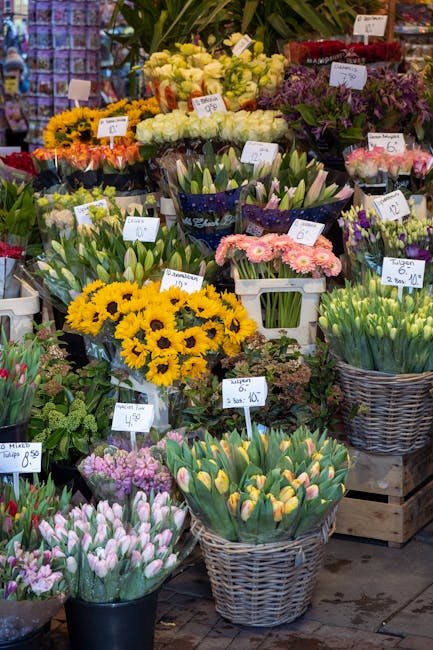 A vibrant display of fresh flowers at Edgware Flowers, featuring yellow sunflowers, pink and purple tulips, white and purple daffodils, and various mixed floral arrangements. The flowers are arranged 